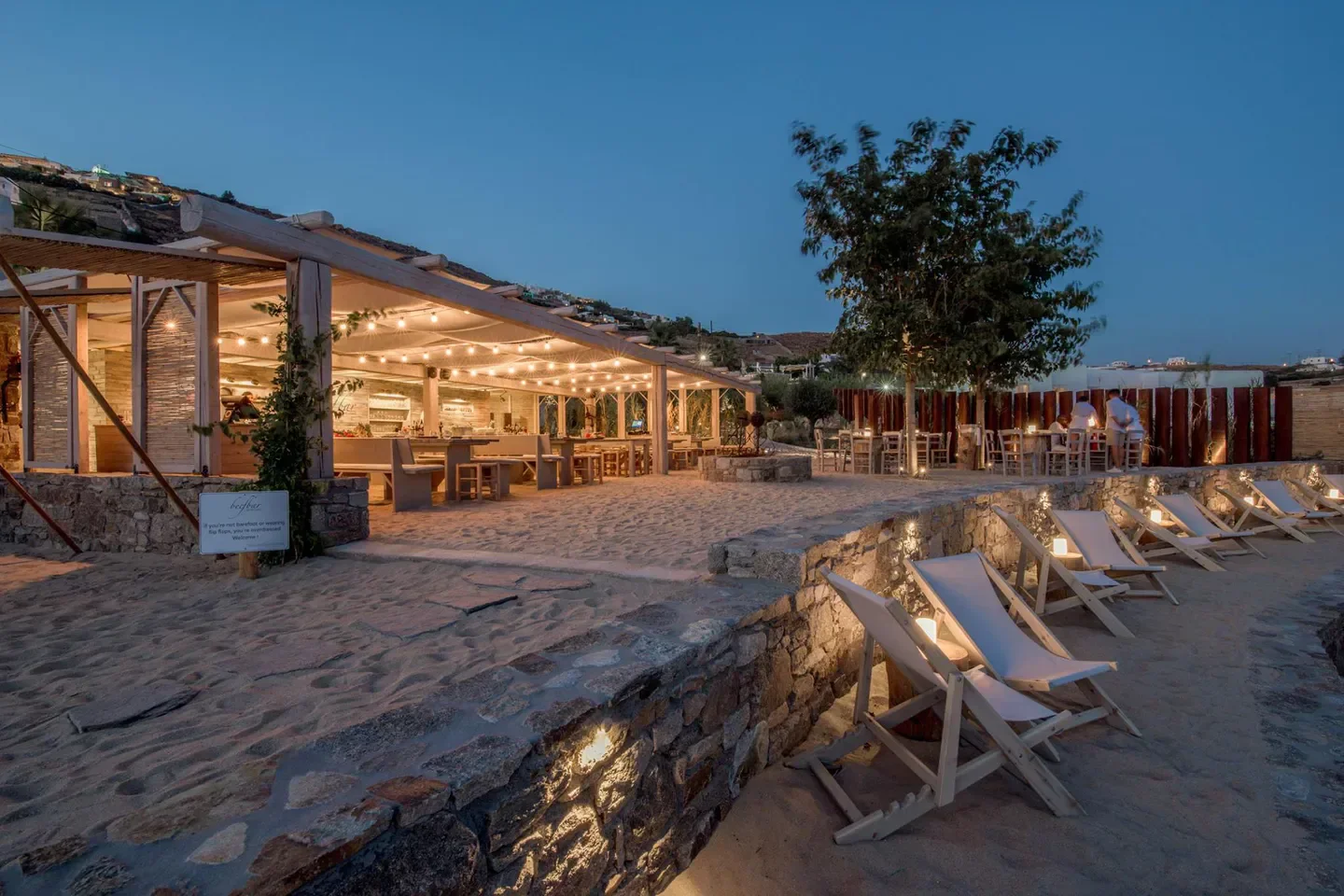 Beachfront evening scene at Beefbar Mykonos, featuring beach chairs and ambient lighting