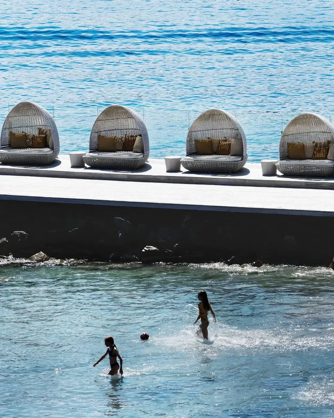 Kids playing in the sea by Buddha Bar Beach in Mykonos, with stylish beachside seating.