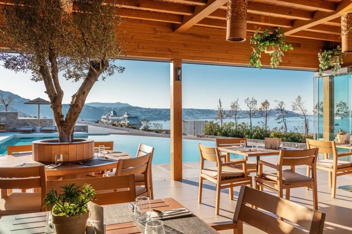 Destino Mykonos restaurant with pool view, olive tree, and sea scenery during daytime