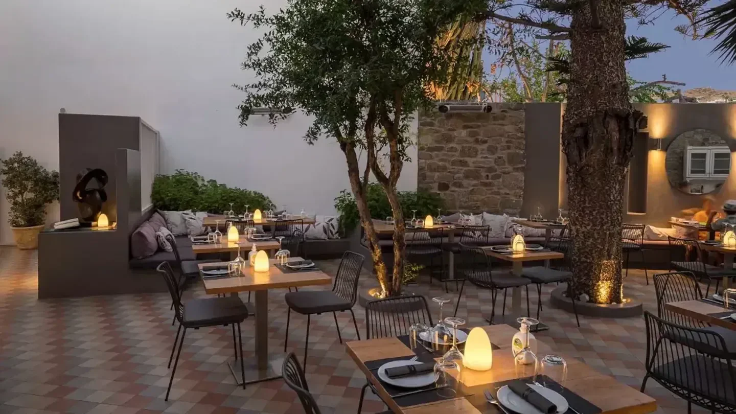 Outdoor dining area at Kalita restaurant in Mykonos, featuring trees and soft lighting.