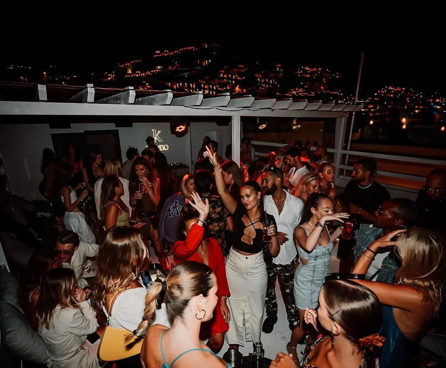 Nightclub scene at Kymbo in Mykonos, featuring a lively crowd and city lights.