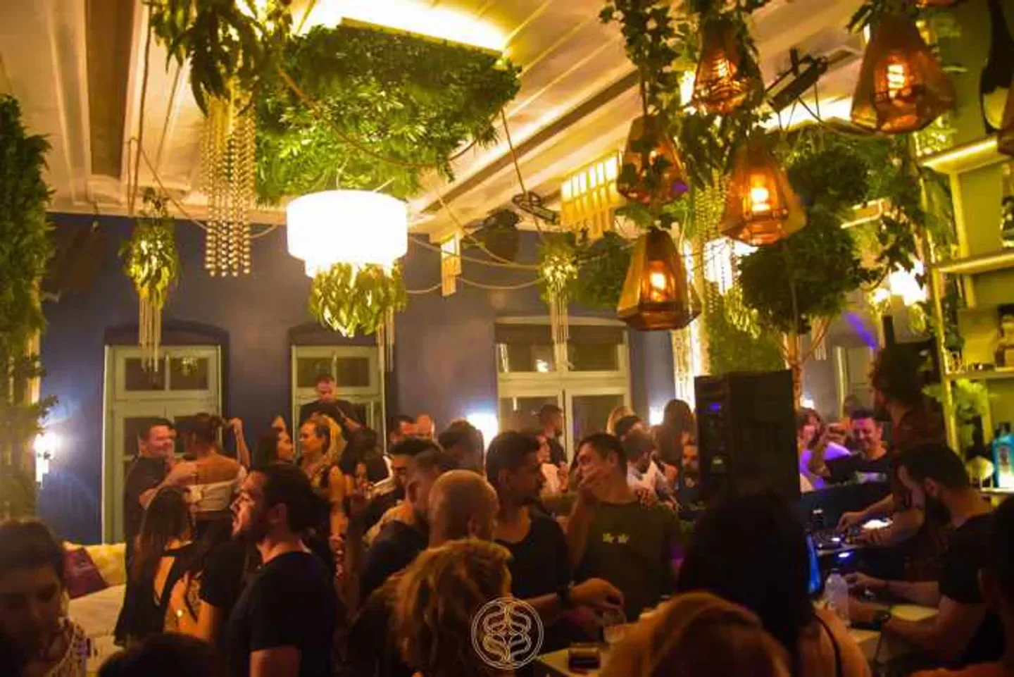 Energetic crowd inside Sanctus nightclub in Mykonos with lush greenery and warm lighting.