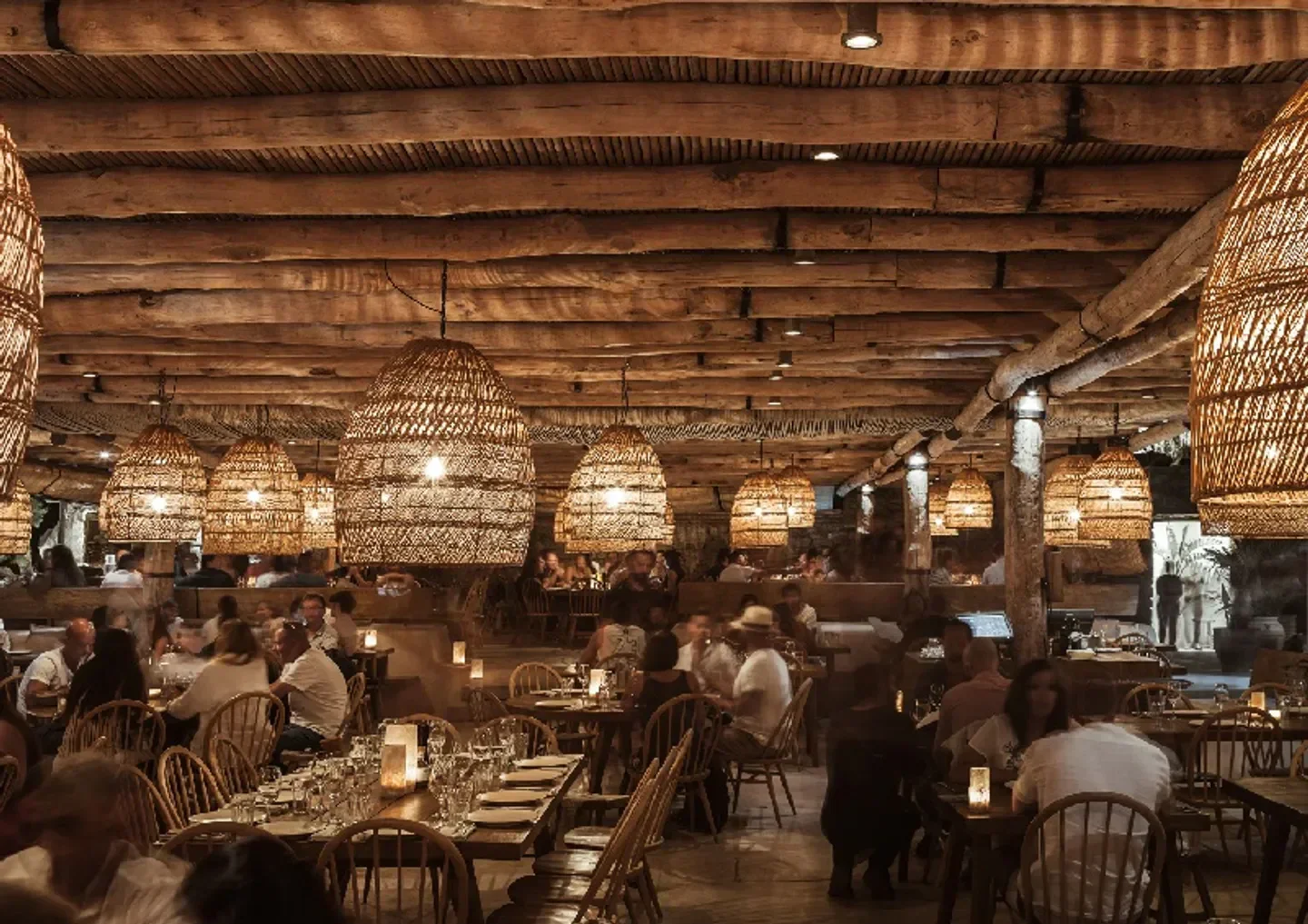 Interior of Scorpios restaurant in Mykonos, featuring woven lamps and a wooden ceiling.