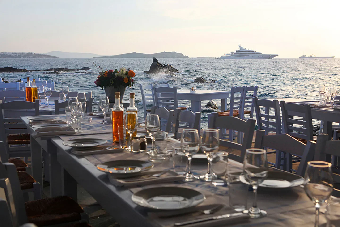 Sea Satin restaurant tables set by the sea in Mykonos, with views of luxury yachts.