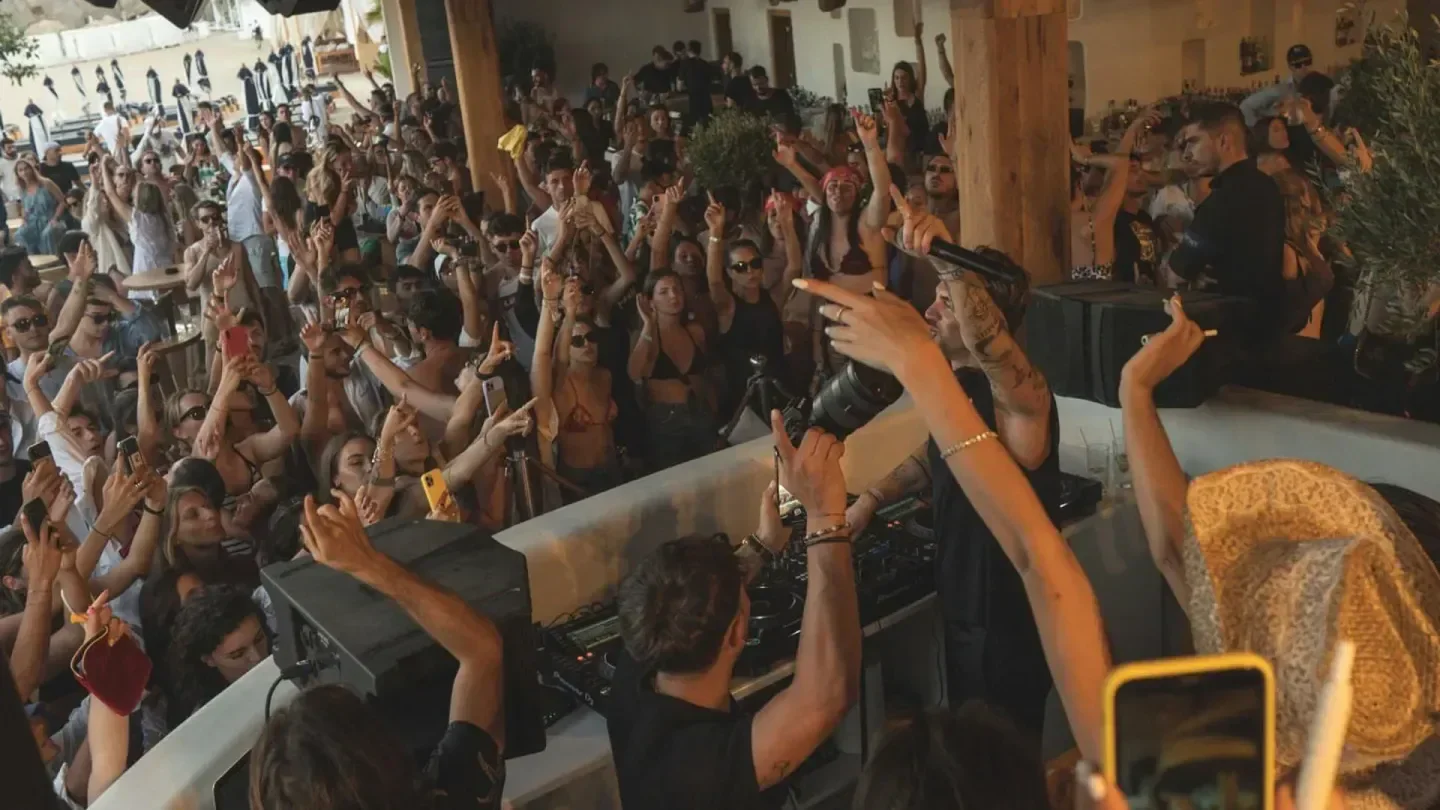 Energetic crowd at Super Paradise beach club in Mykonos, dancing to the DJ's music.